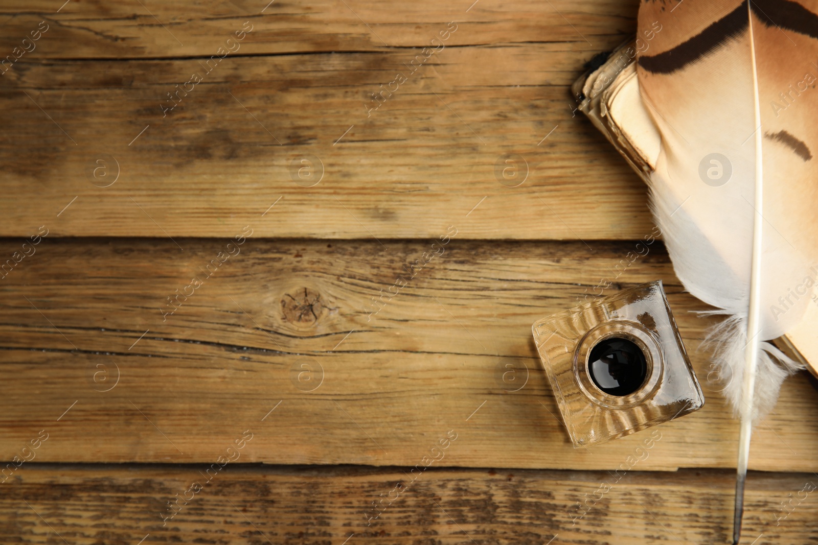 Photo of Feather pen, inkwell and old book on wooden table, flat lay. Space for text