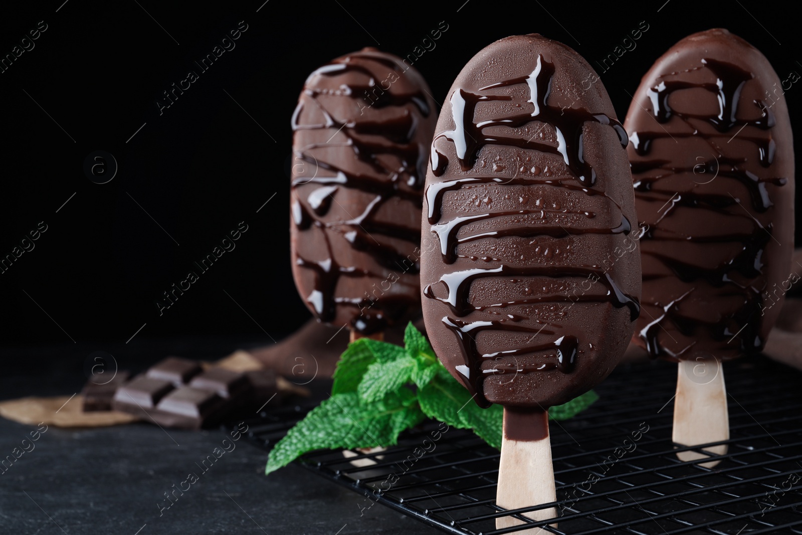 Photo of Delicious glazed ice cream bars and mint on black table. Space for text