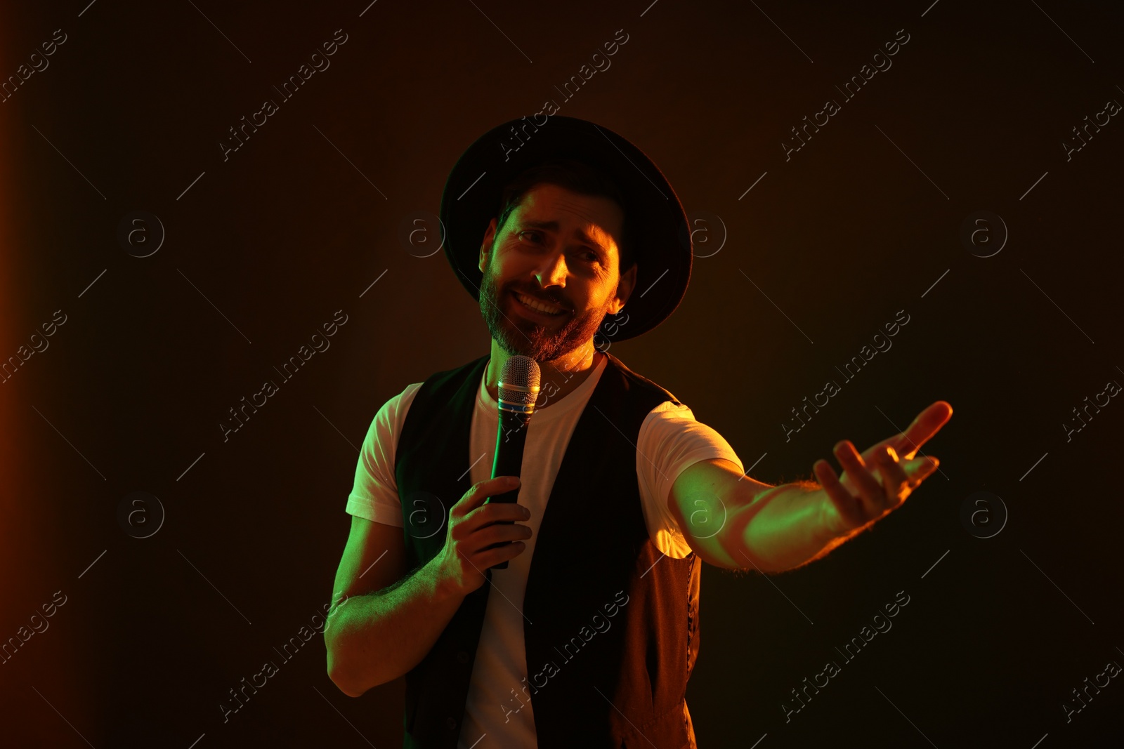 Photo of Handsome man with microphone singing in neon lights on dark background