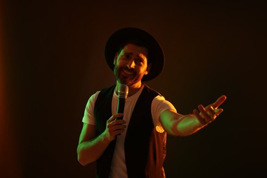 Photo of Handsome man with microphone singing in neon lights on dark background