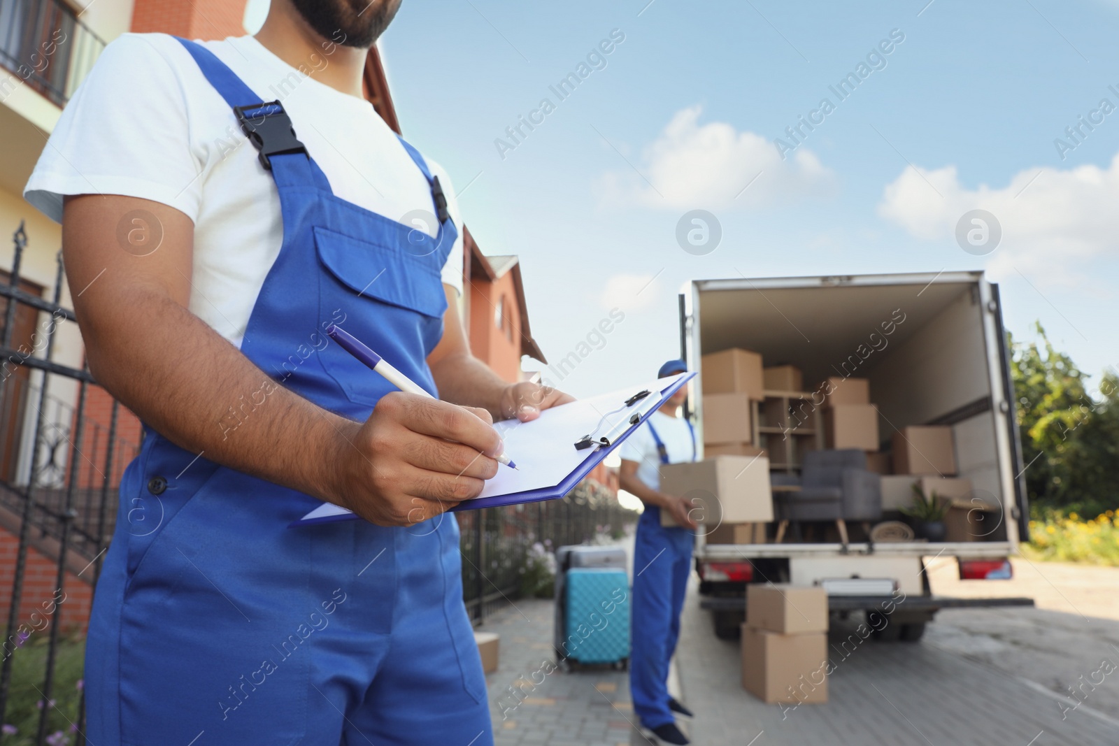 Photo of Moving service workers outdoors, unloading boxes and checking list