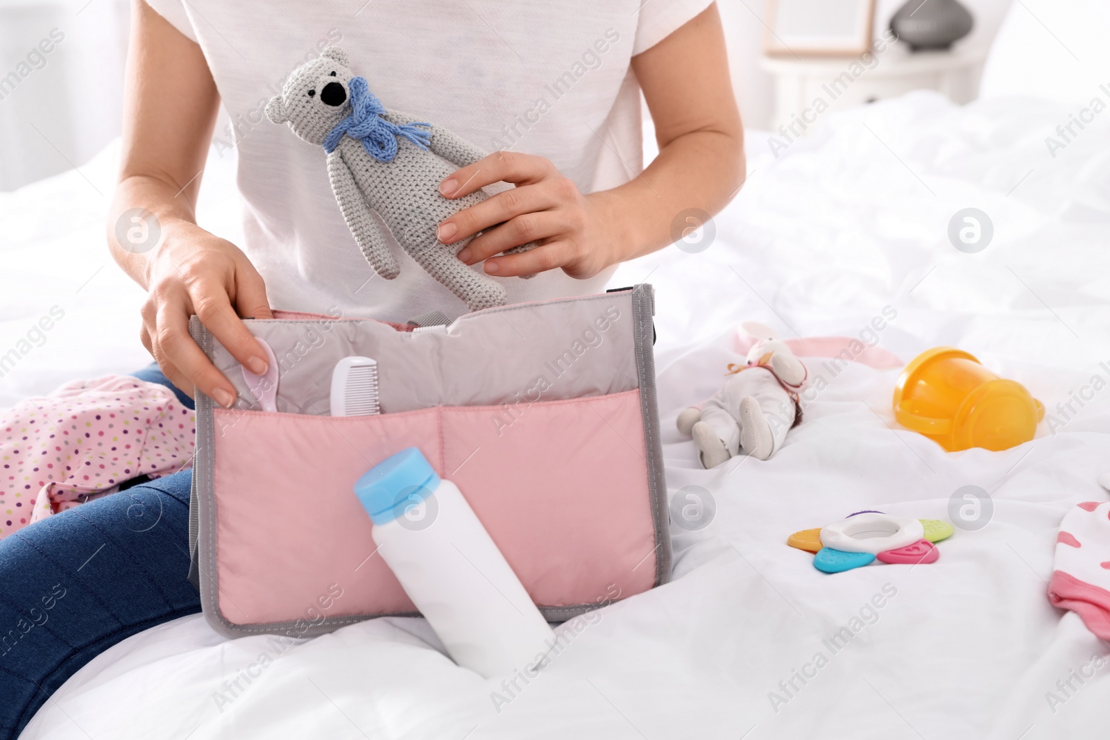 Photo of Woman packing baby accessories into maternity bag on bed, closeup