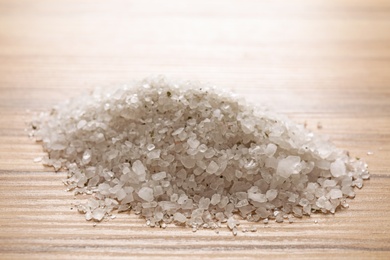 Photo of Pile of white sea salt for spa scrubbing procedure on wooden table