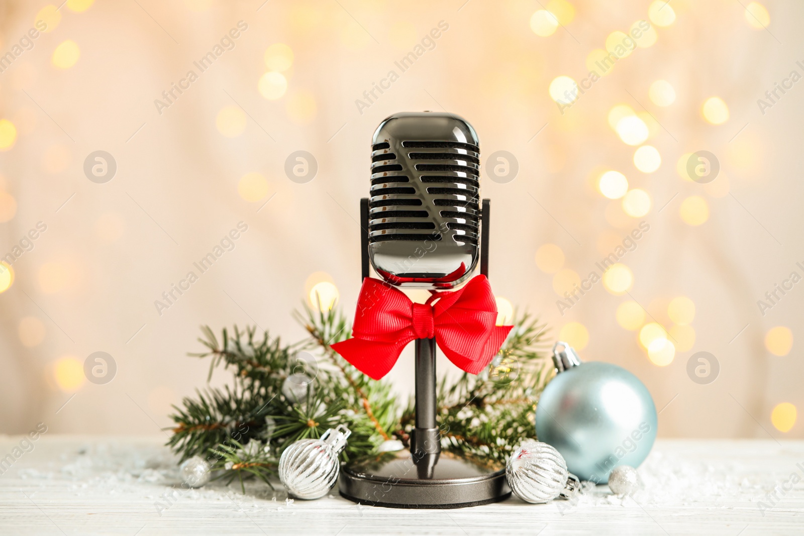 Photo of Microphone with red bow and decorations on white table against blurred lights. Christmas music