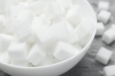 Photo of White sugar cubes in bowl on grey table, closeup