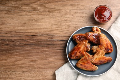 Photo of Delicious fried chicken wings and sauce served on wooden table, flat lay. Space for text