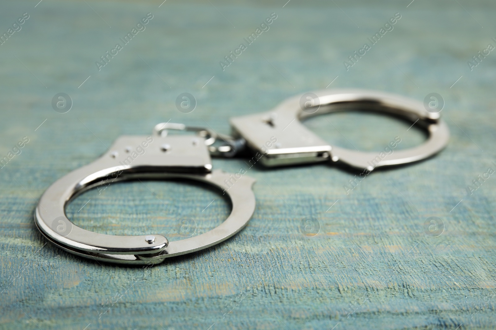 Photo of Classic chain handcuffs on blue wooden table, closeup