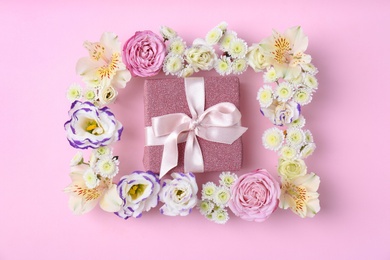 Photo of Frame of flowers and gift box on color background, top view