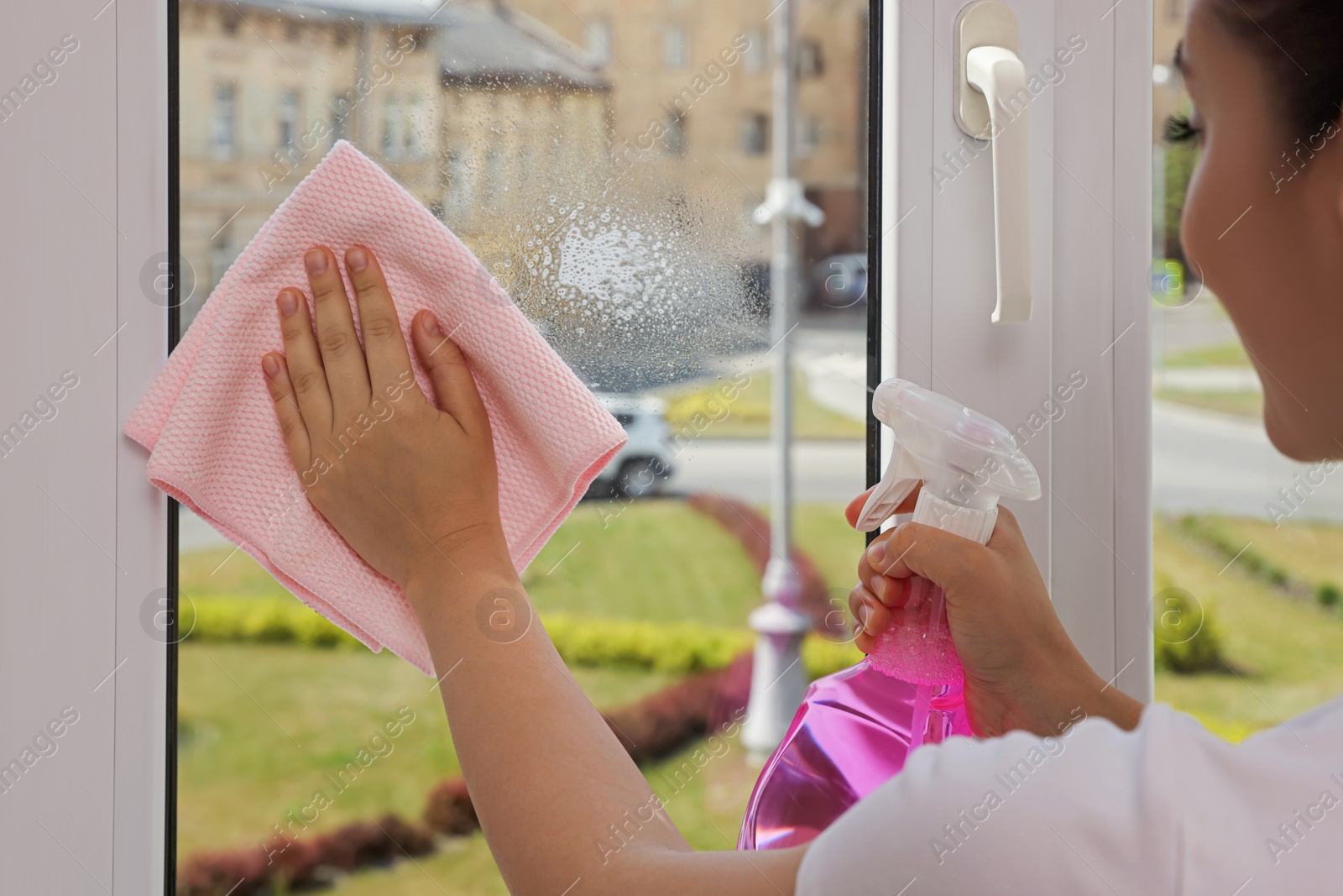 Photo of Young woman cleaning window glass with rag and detergent at home, closeup