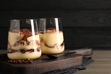 Photo of Delicious tiramisu in glasses, spoon and coffee beans on wooden table. Space for text