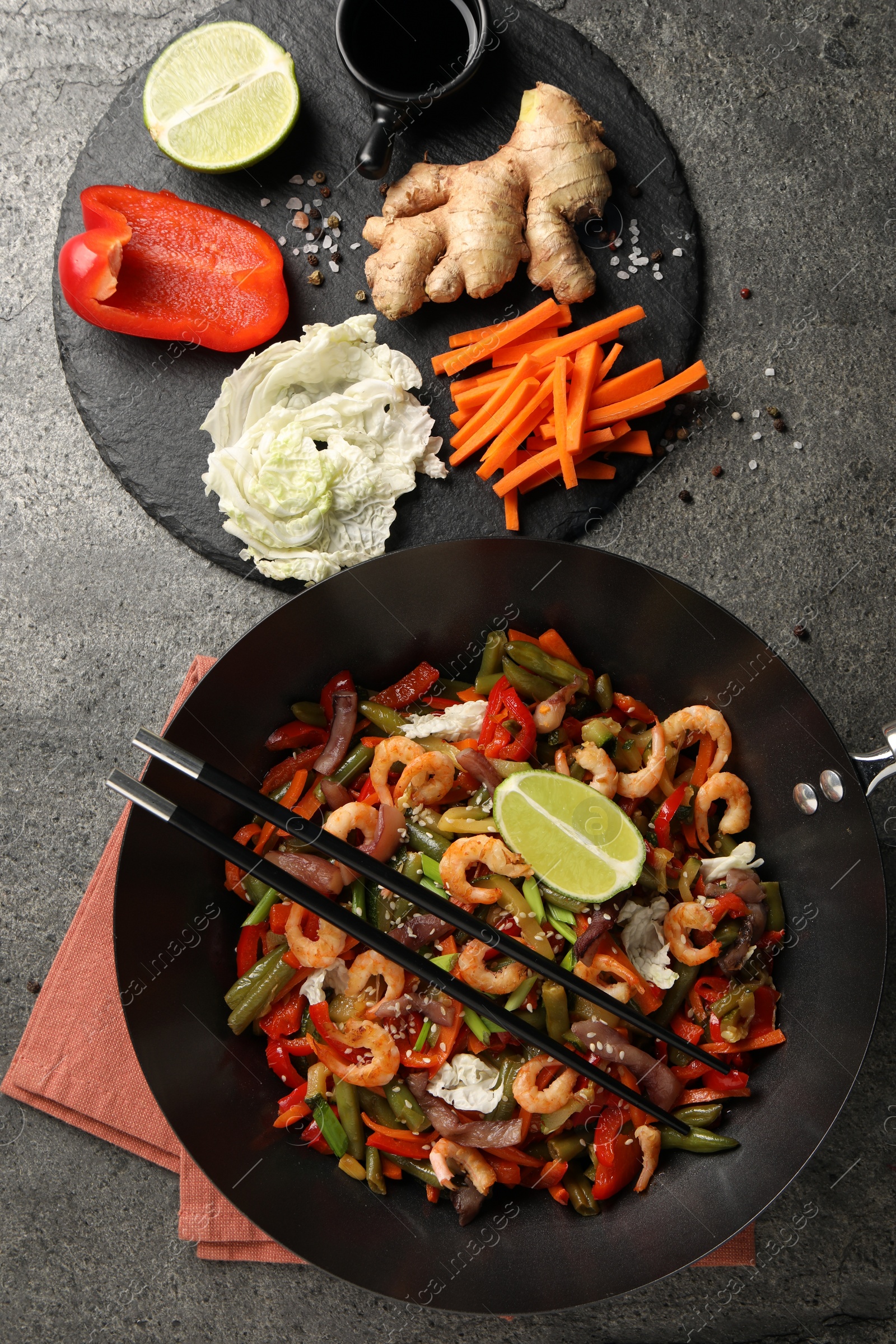 Photo of Shrimp stir fry with vegetables in wok and chopsticks on grey table, flat lay