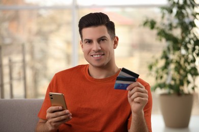 Photo of Man using smartphone and credit card for online payment at home