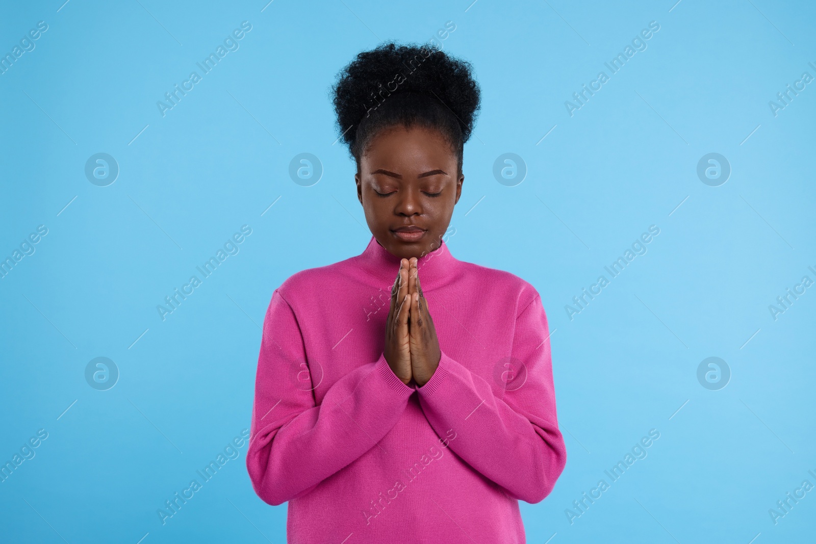 Photo of Woman with clasped hands praying to God on light blue background