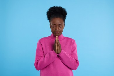 Woman with clasped hands praying to God on light blue background