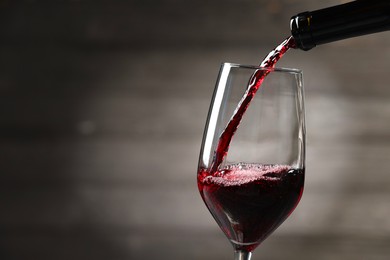 Photo of Pouring red wine into glass against gray background, closeup. Space for text