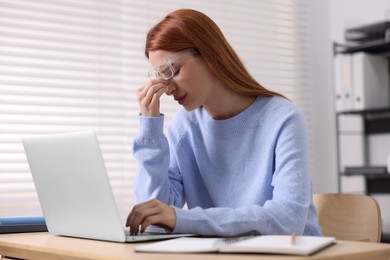 Woman in glasses suffering from headache at workplace in office