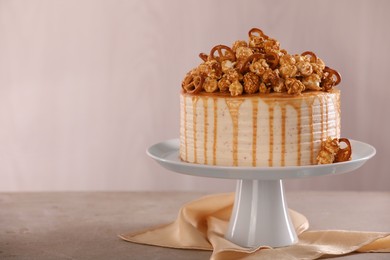 Photo of Caramel drip cake decorated with popcorn and pretzels on light grey table, space for text