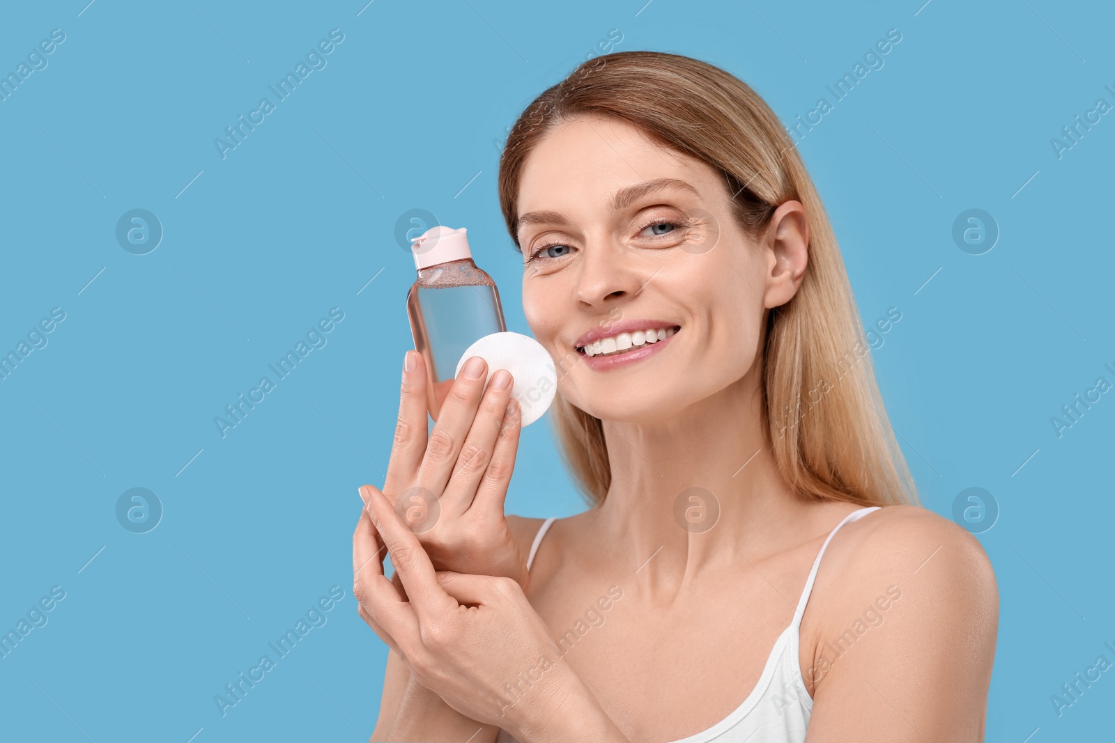 Photo of Beautiful woman with makeup remover and cotton pad on light blue background, space for text