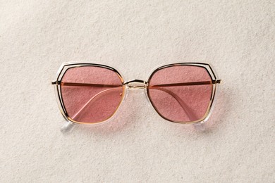 Photo of New stylish sunglasses on sand, top view