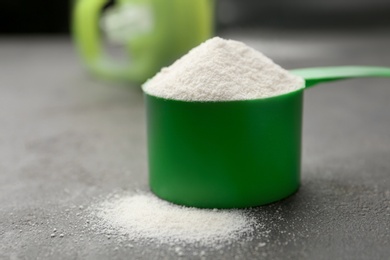 Photo of Measuring scoop of protein powder on grey stone table, closeup