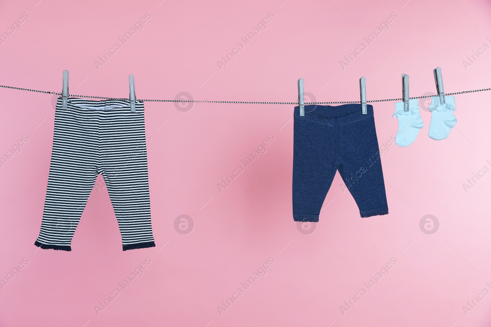 Photo of Different baby clothes drying on laundry line against pink background