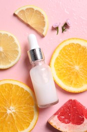 Photo of Bottle of cosmetic serum, sliced citrus fruits and small flowers on wet pink background, flat lay