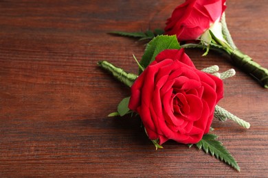 Photo of Two stylish red boutonnieres on wooden table, space for text
