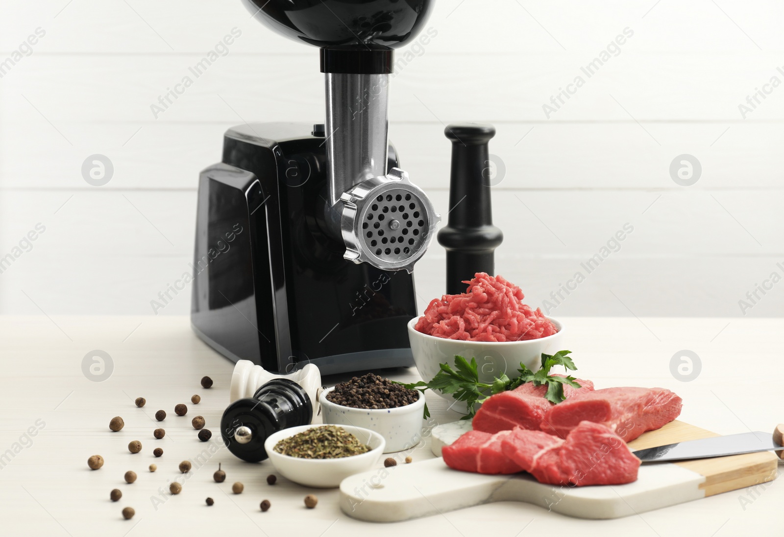 Photo of Meat grinder, beef, parsley and spices on white table