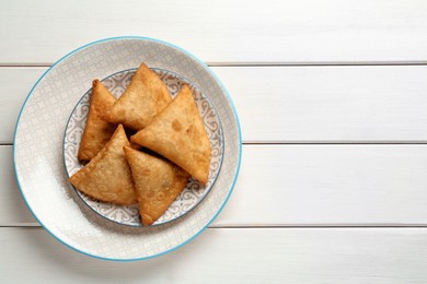 Photo of Fresh delicious crispy samosas on white wooden table, top view. Space for text