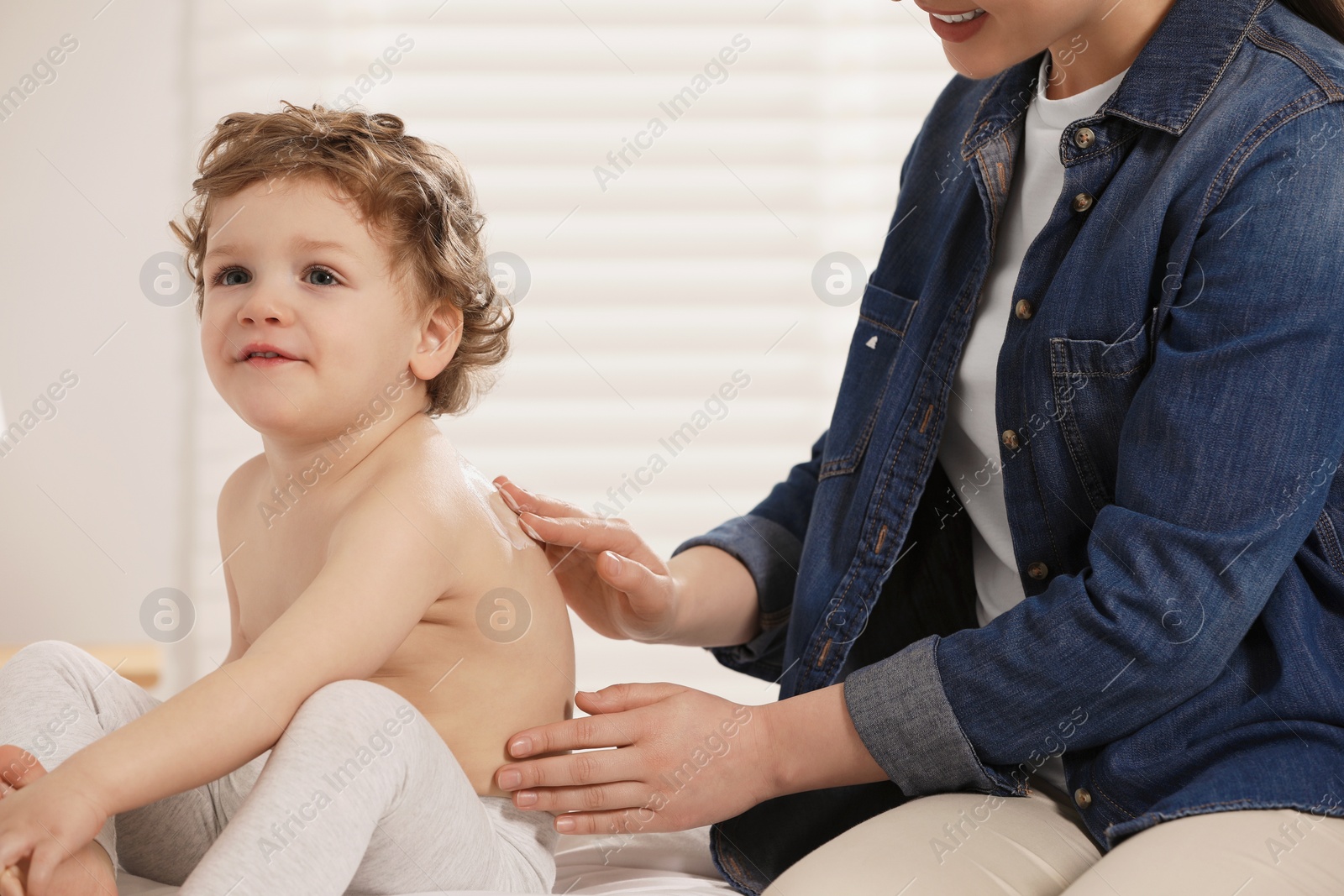 Photo of Mother applying ointment onto her son`s back on bed indoors