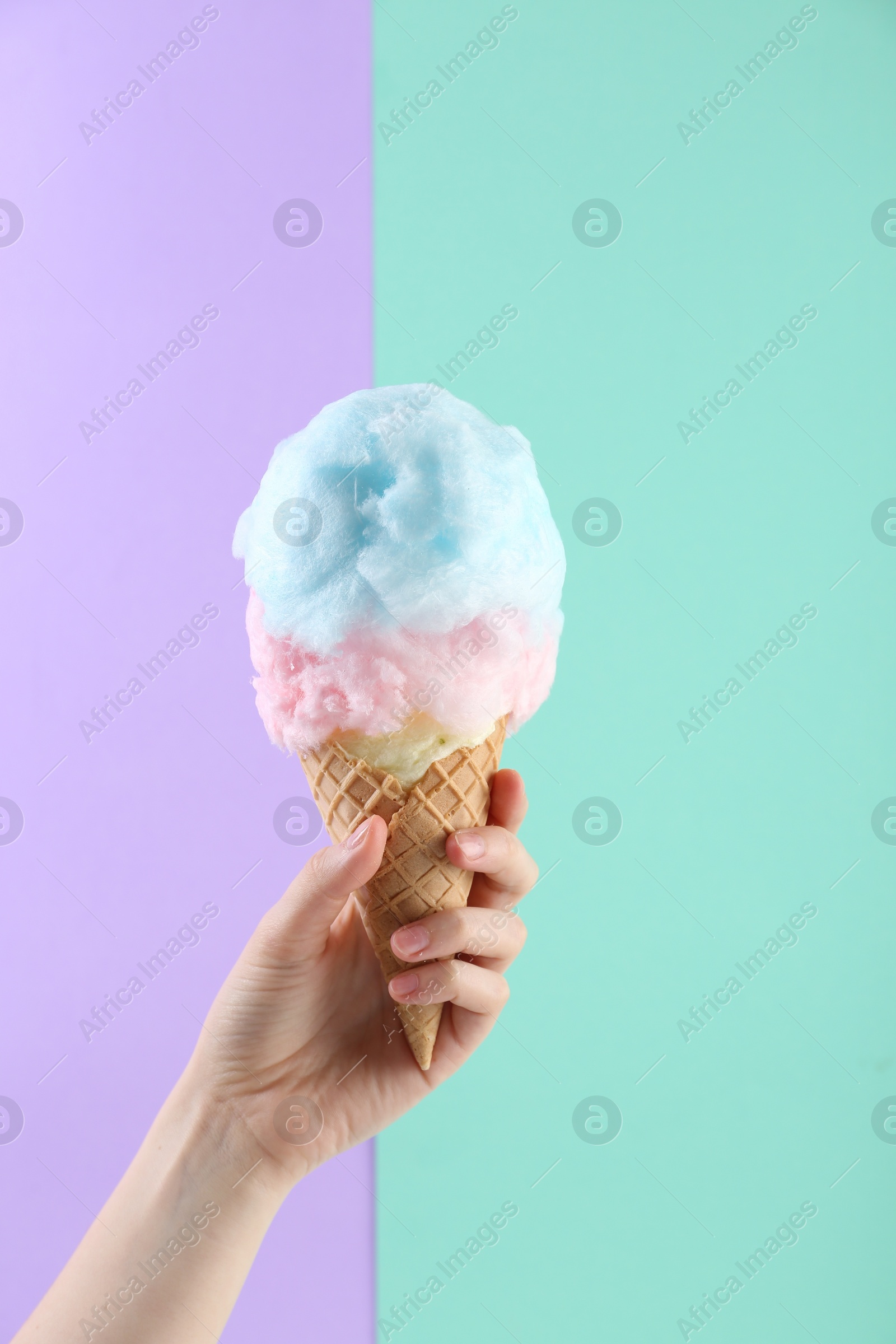 Photo of Woman holding waffle cone with cotton candy on color background, closeup