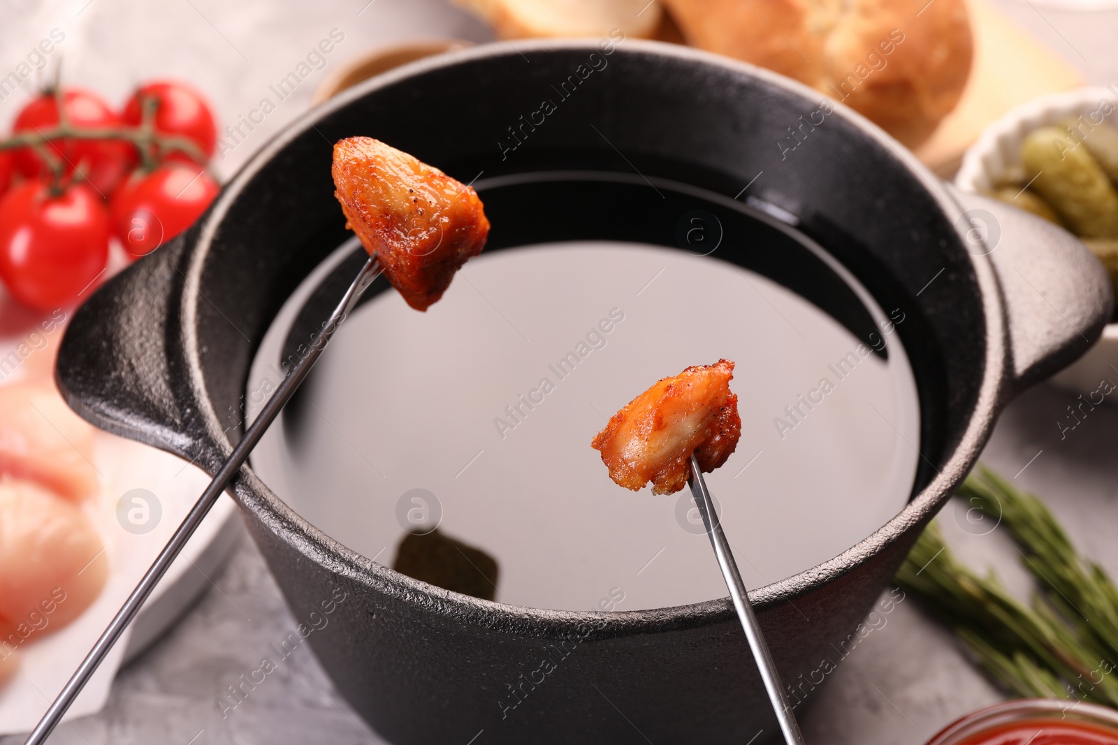 Photo of Fondue pot, forks with fried meat pieces and other products on grey textured table, closeup