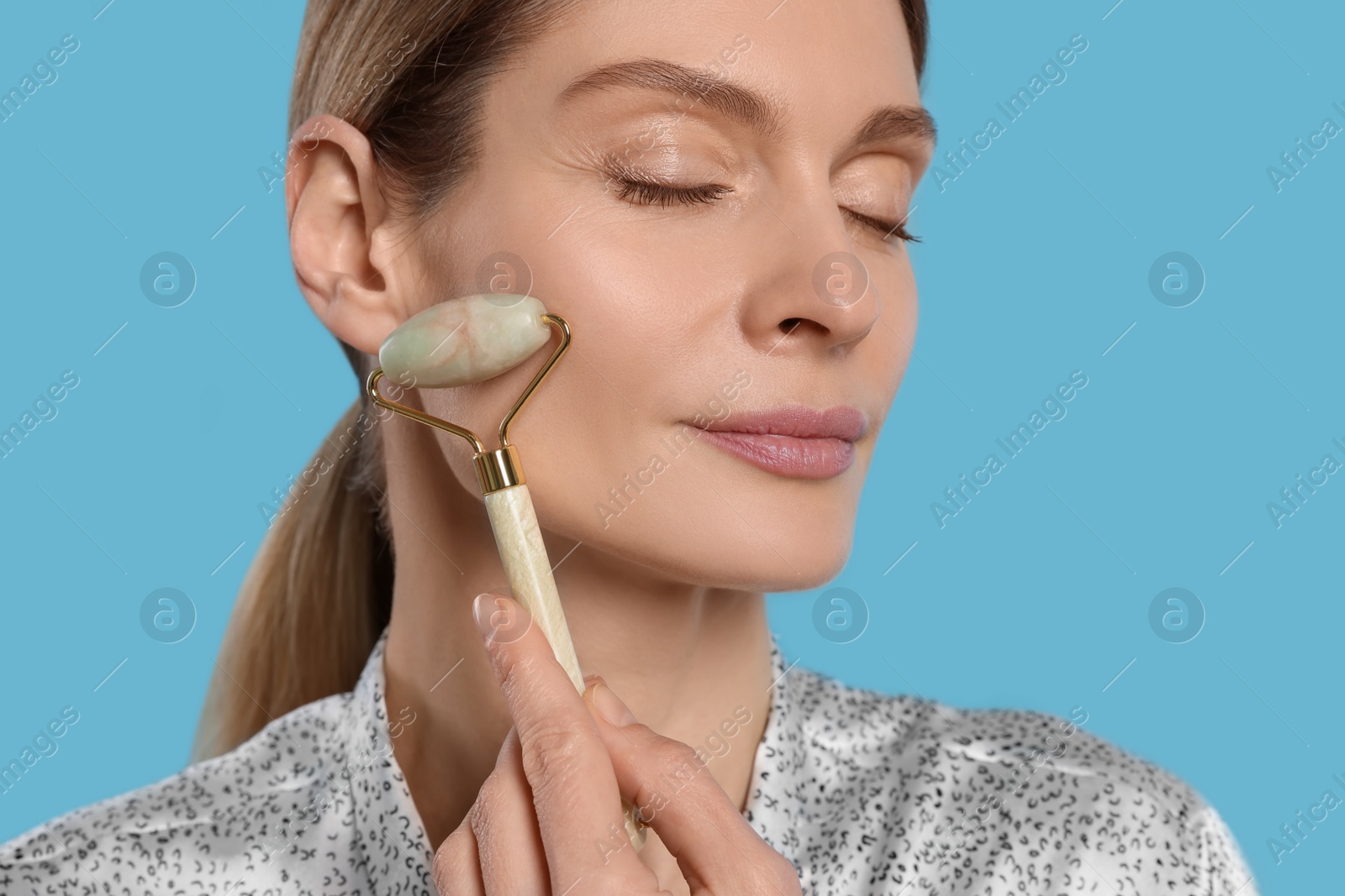 Photo of Woman massaging her face with jade roller on turquoise background