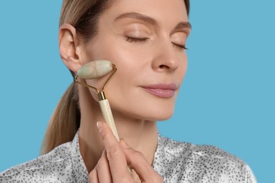 Photo of Woman massaging her face with jade roller on turquoise background