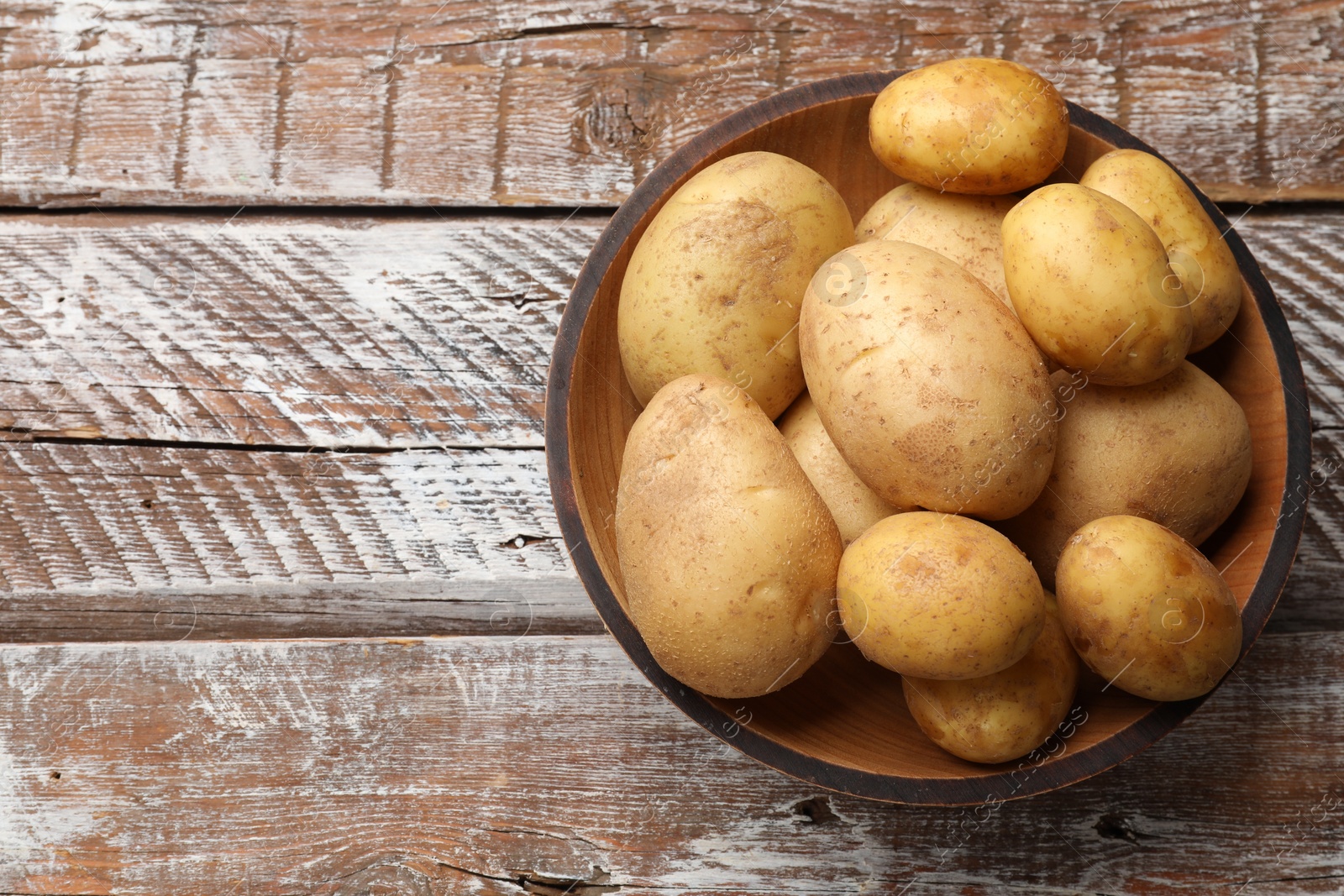 Photo of Raw fresh potatoes in bowl on wooden table, top view. Space for text