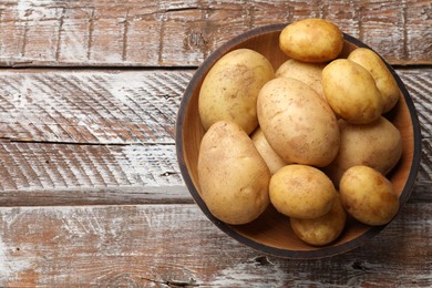 Photo of Raw fresh potatoes in bowl on wooden table, top view. Space for text