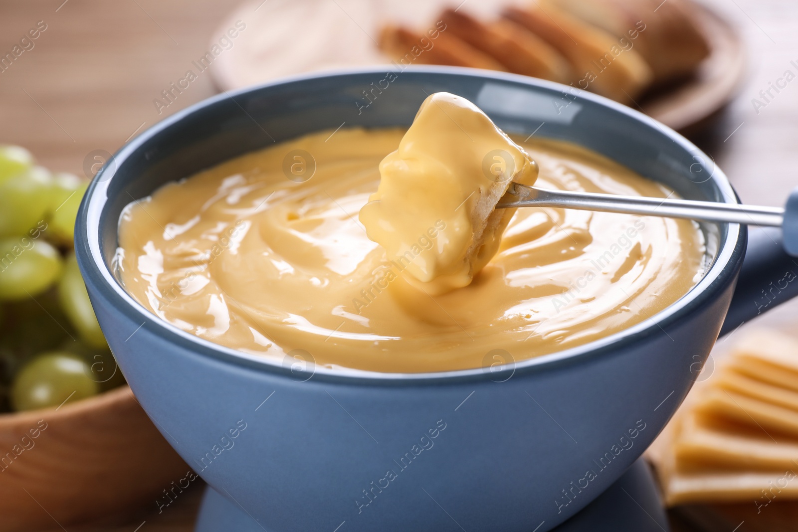 Photo of Dipping bread into pot with cheese fondue on table, closeup