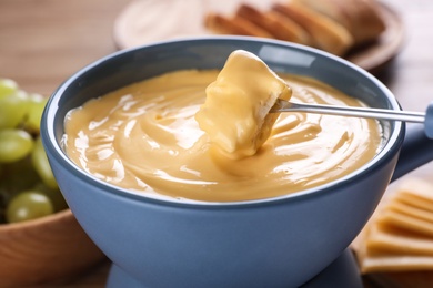 Dipping bread into pot with cheese fondue on table, closeup