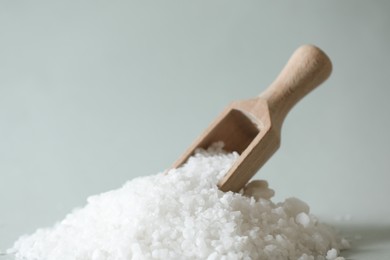 Photo of Organic salt and wooden scoop on light grey background, closeup. Space for text