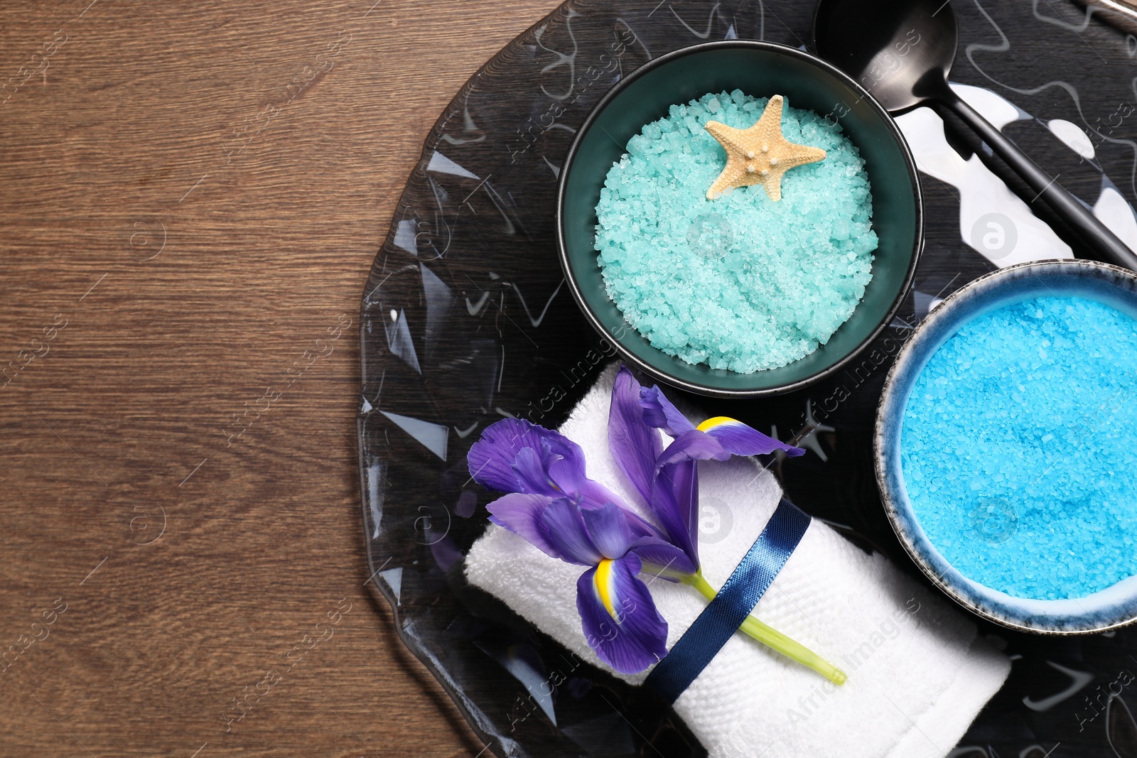 Photo of Light blue sea salt in bowls, flower, towel and starfish on wooden table, top view. Space for text