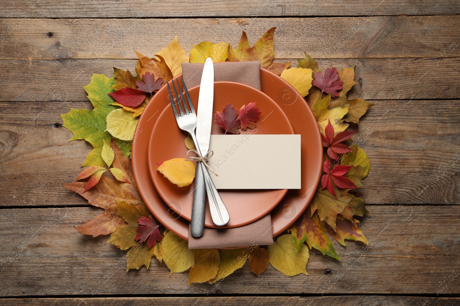 Photo of Festive table setting with autumn leaves and blank card on wooden background, flat lay