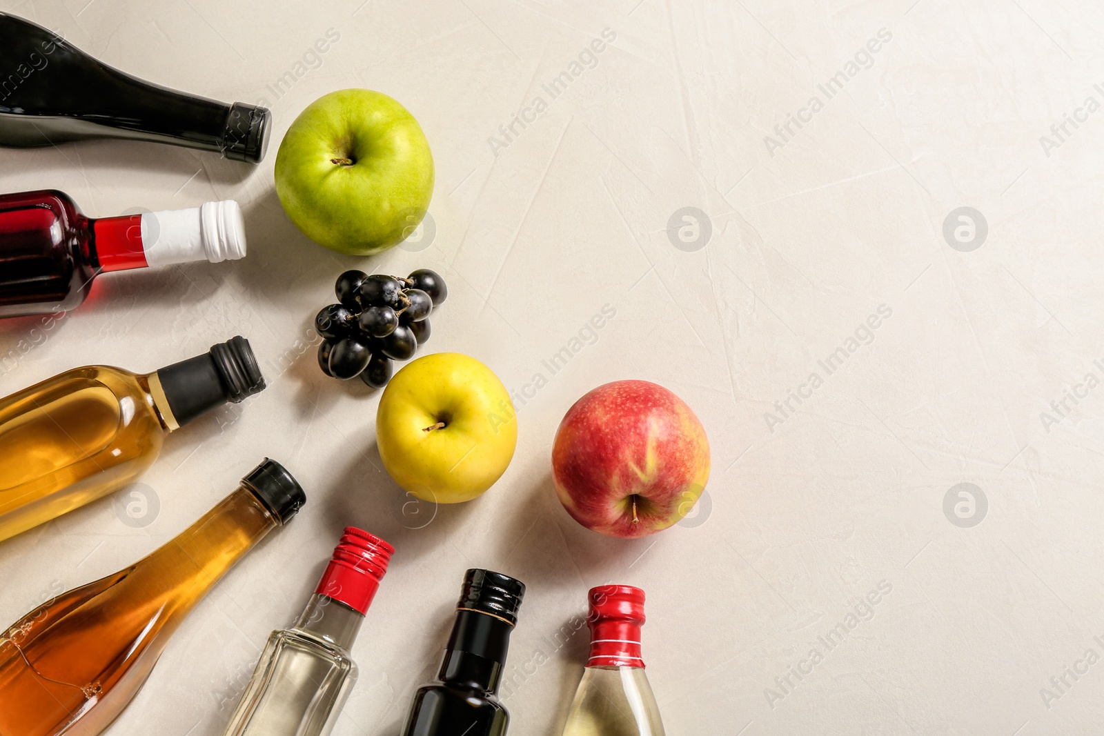 Photo of Flat lay composition with different kinds of vinegar in bottles and space for text on light background