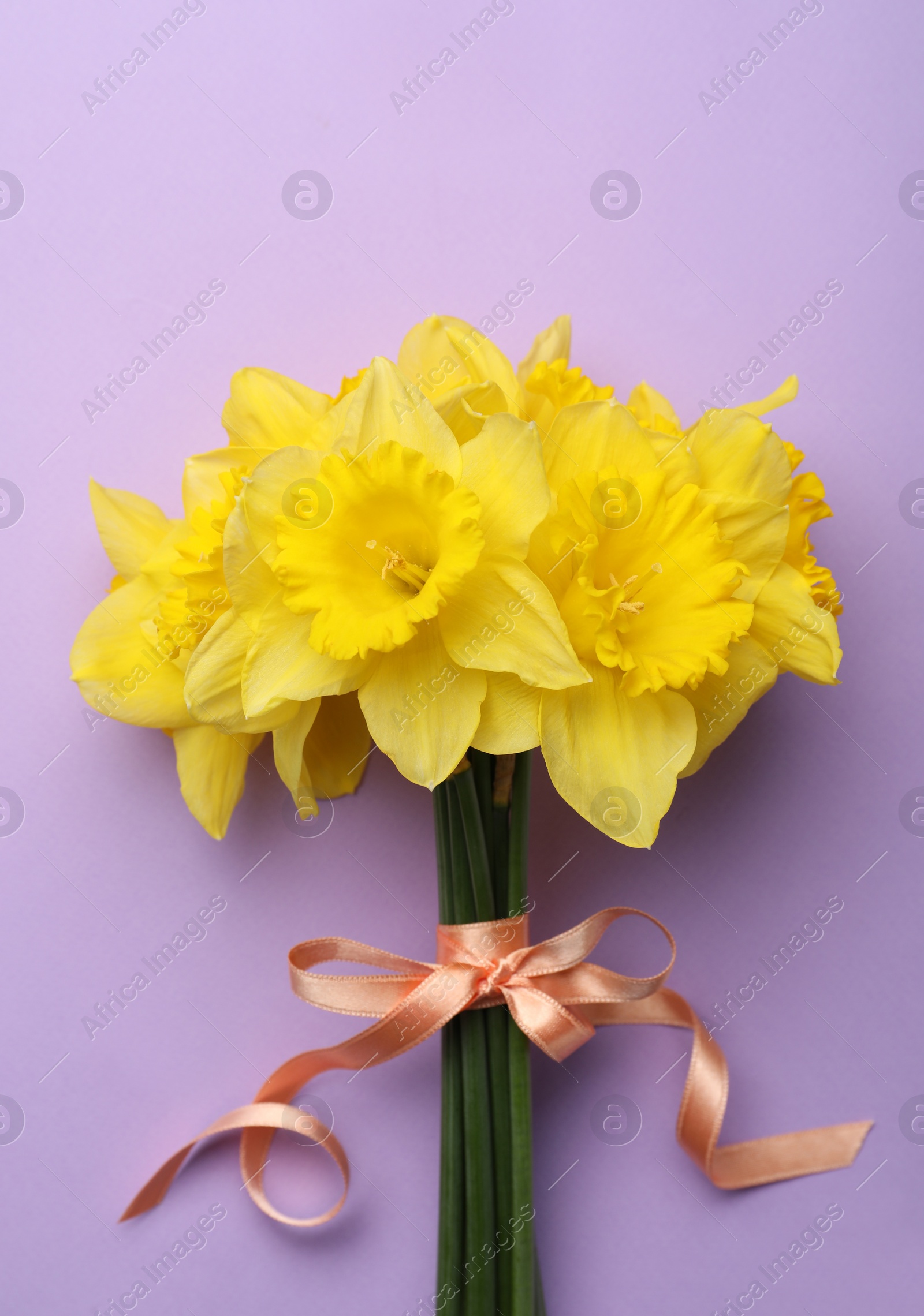 Photo of Beautiful daffodil bouquet on violet background, top view