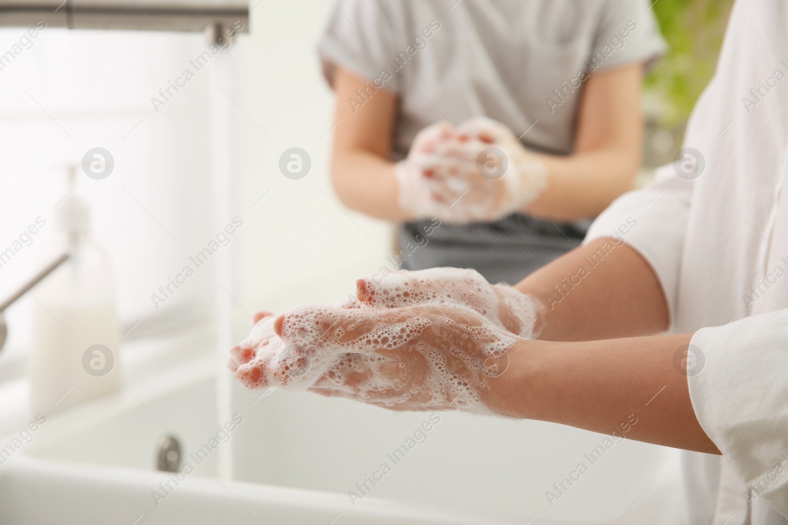 Photo of Mother and daughter washing hands with liquid soap in kitchen, closeup