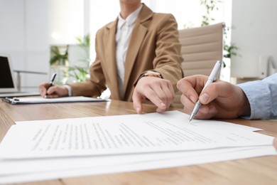 Photo of Businesspeople signing contract at table in office, closeup