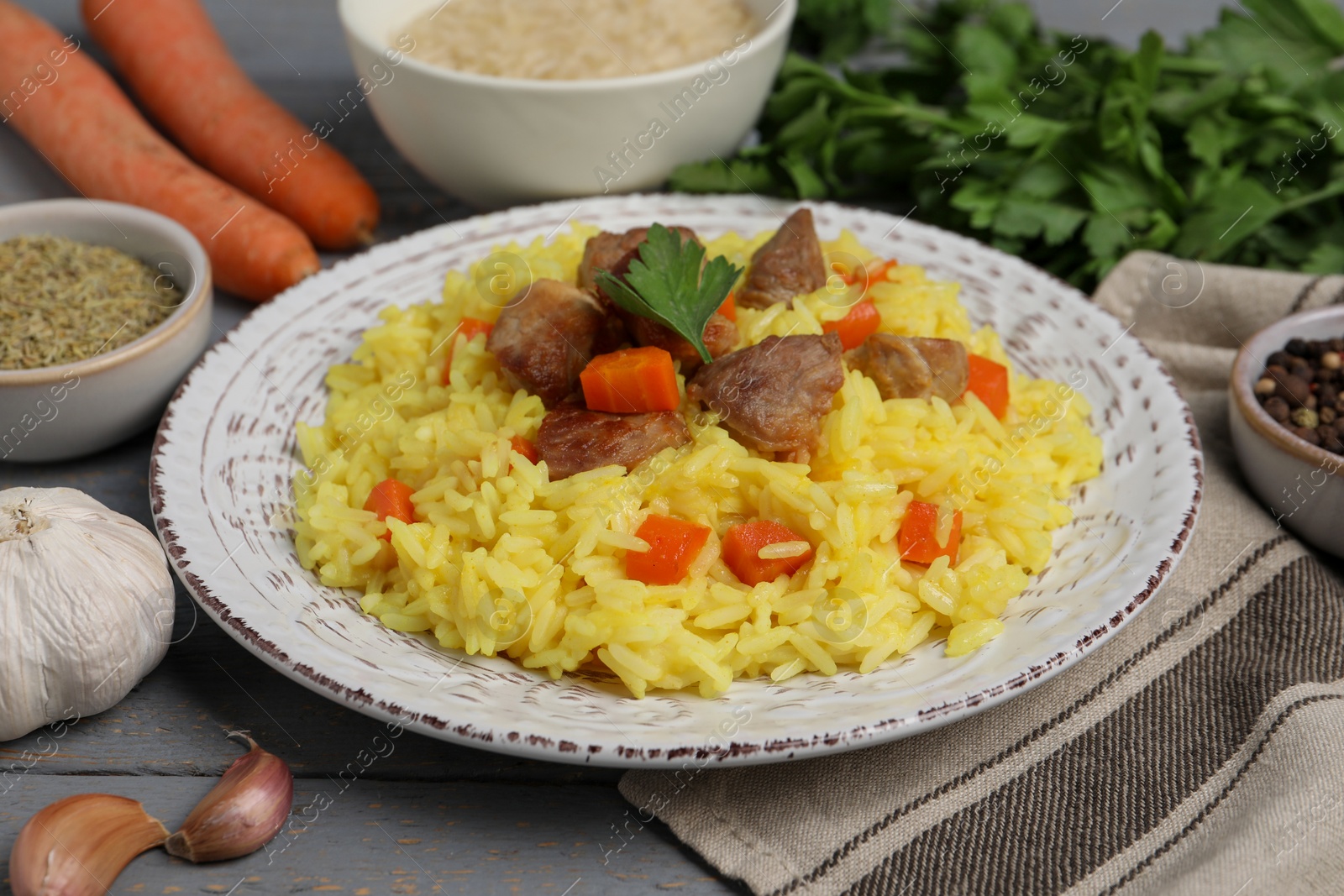 Photo of Delicious pilaf with meat and ingredients on grey wooden table, closeup