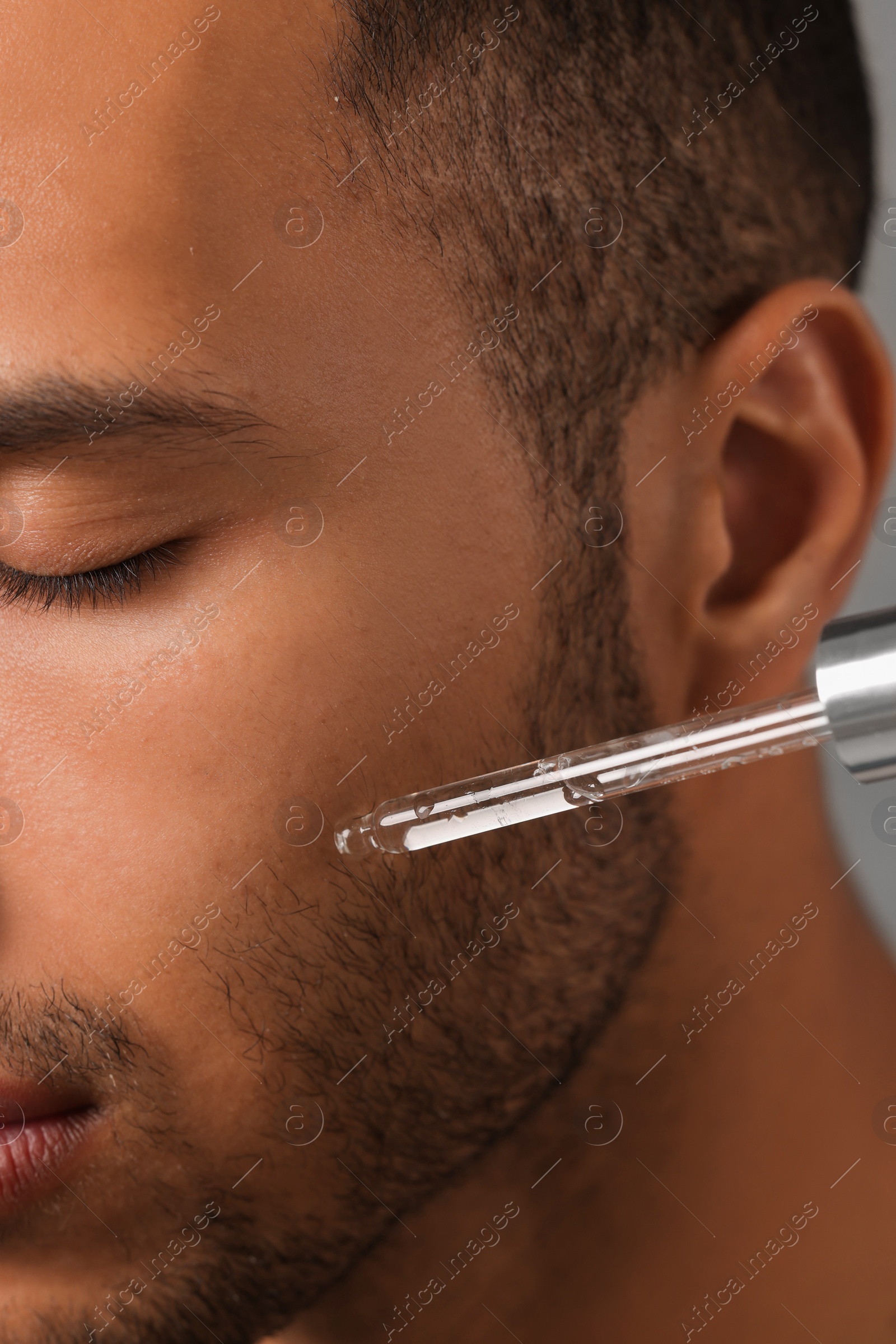 Photo of Man applying cosmetic serum onto face, closeup