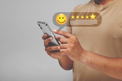 Man leaving service feedback with smartphone on light background, closeup. Stars and emoticon over device