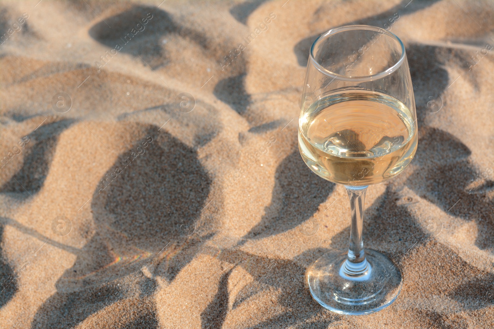 Photo of Glass of tasty wine on sand, space for text