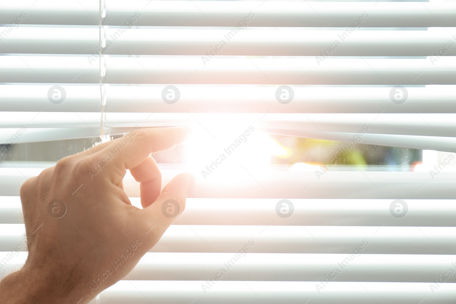 Photo of Young man opening window blinds, closeup. Space for text